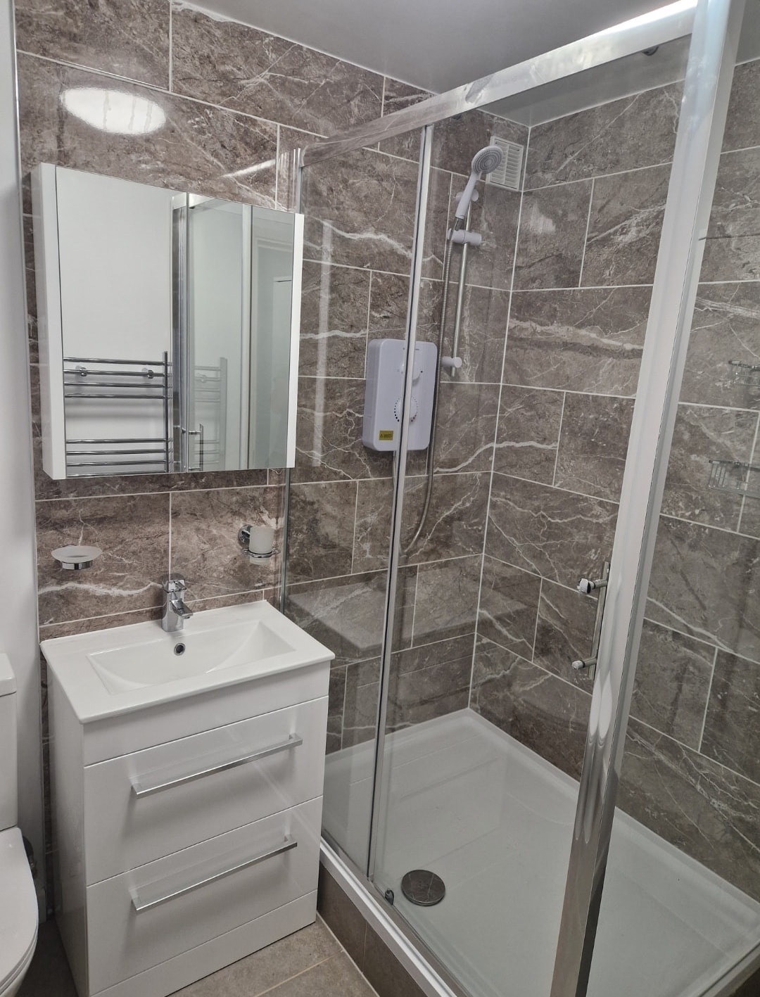 Bathroom refurbishment with updated plumbing, a new shower enclosure and dark marble-effect tiling. The photo shows the shower and basin area.