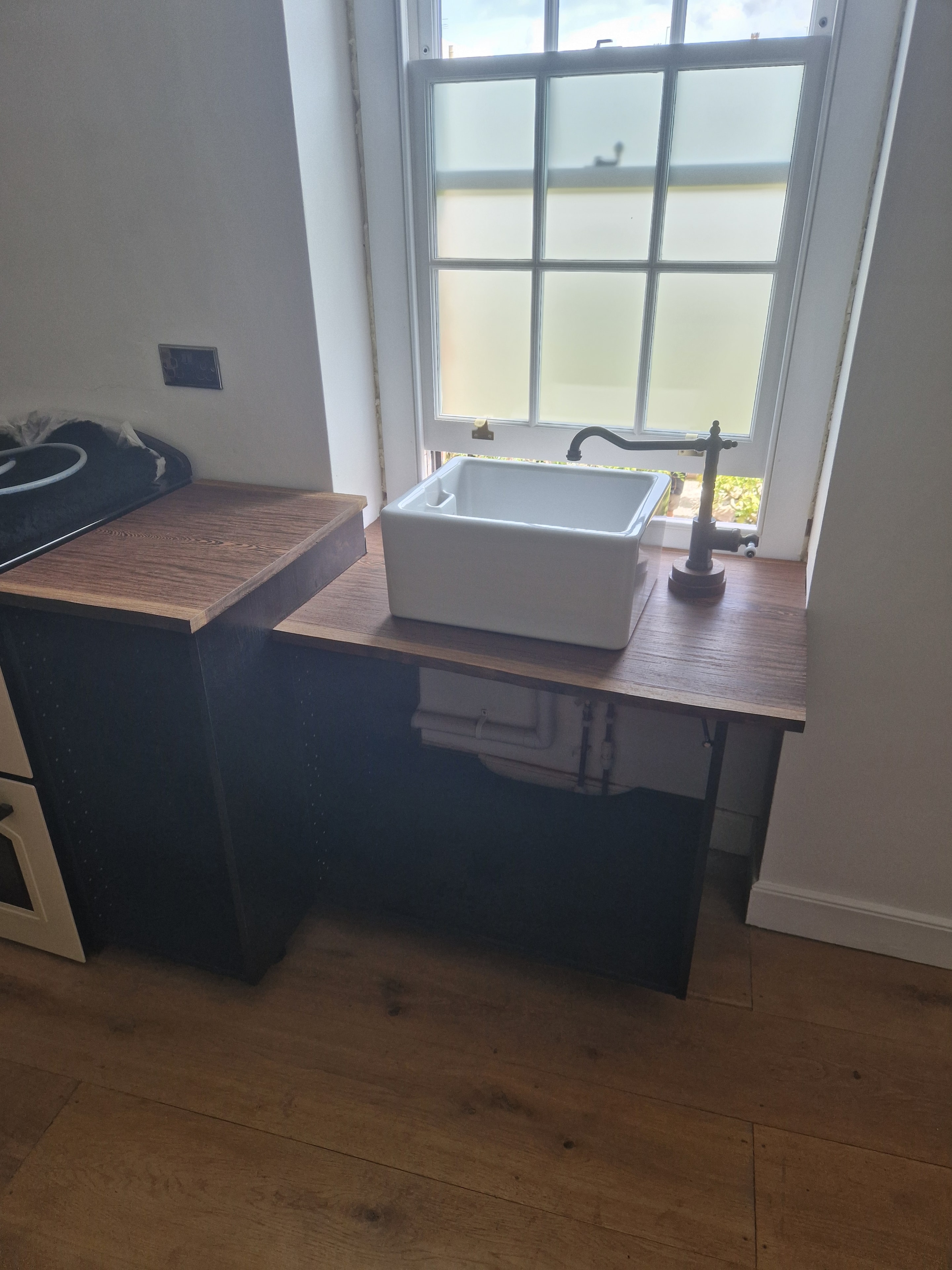 Custom timber worktop with a raised section, fitted around a ceramic sink beneath the window.