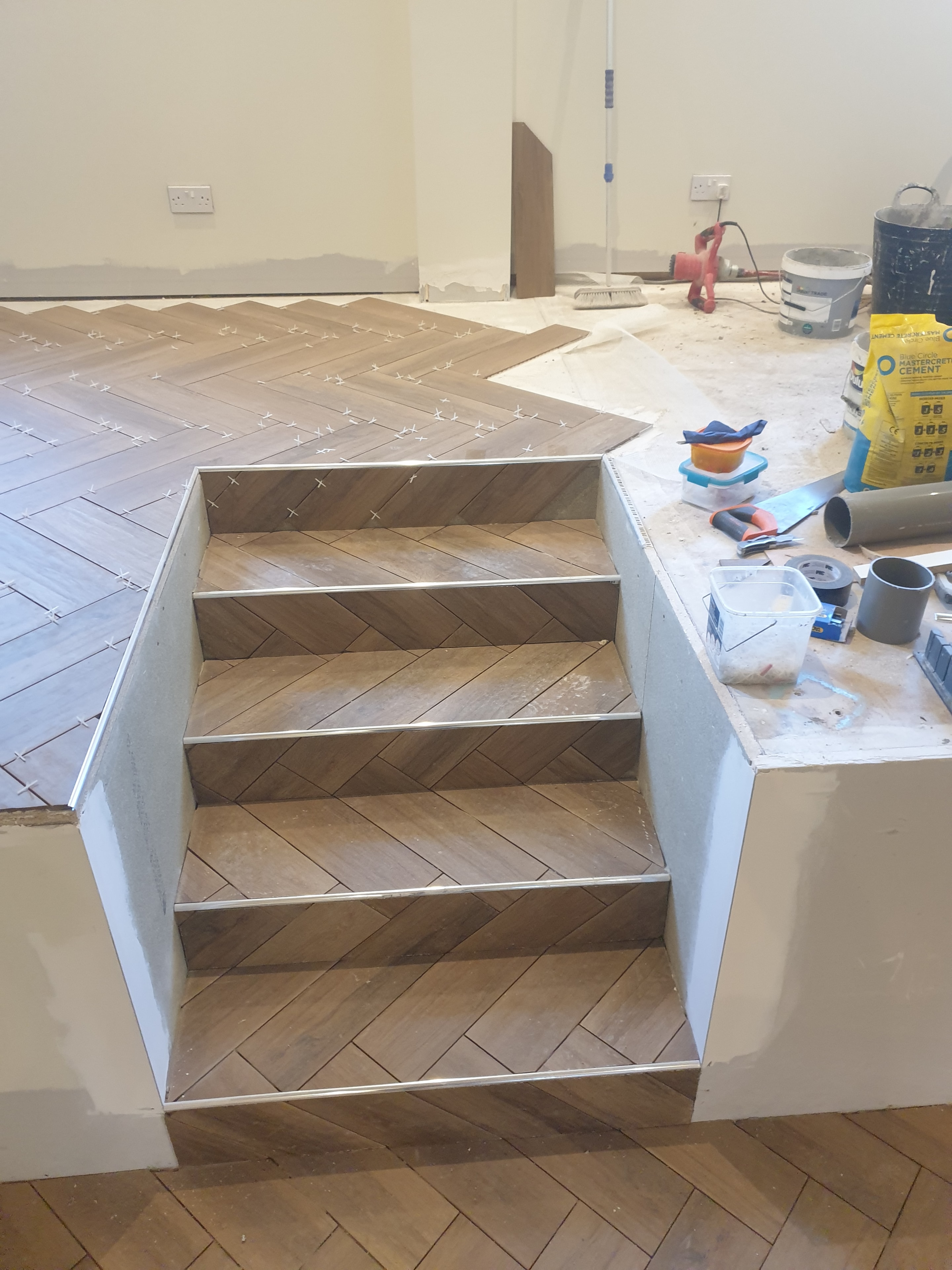Tiling in progress across a raised floor and steps, with the tile pattern carried through each stair riser.